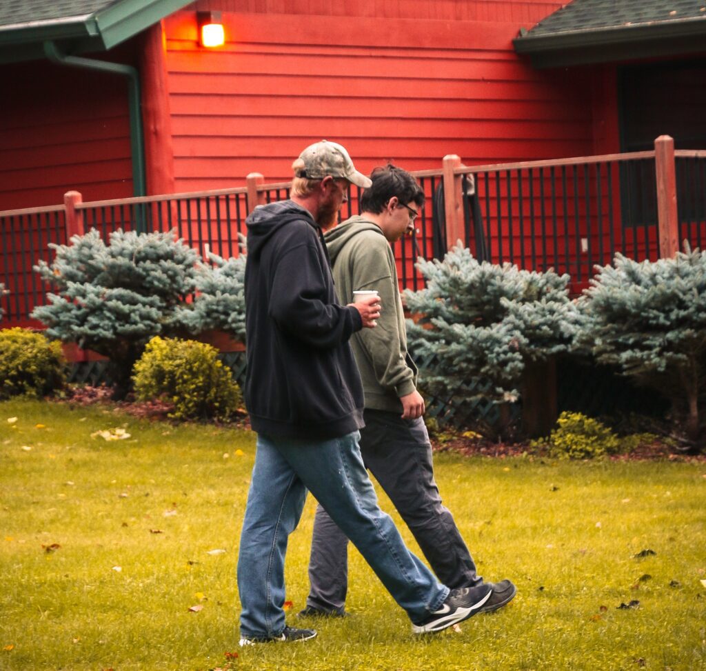 Adult man walking with teen boy on green grass with a red house in the background